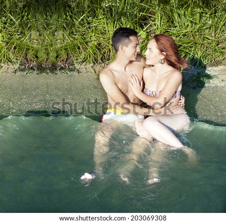 young adult caucasian embracing couple in love at sand tropical beach background Copy space for inscription Beautiful man and woman sitting in clear blue water with wave Copy space for inscription