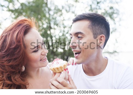 Close up portrait of man and woman feed each other delicious sweet cakes outdoors at picnic