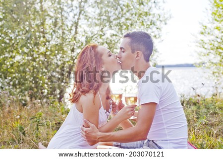 Portrait of Young couple on a picnic with wine Man and woman kissing outdoor on summer fresh green grass and trees background Copy space for inscription