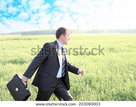Portrait of active well dressed Businessman walks with black suitcase in fresh green grass field go to future ahead Copy space for inscription