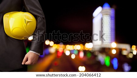 torso engineer or worker holding in hand yellow plastic helmet for workers security over  high-rise buildings and night road with bokeh light background