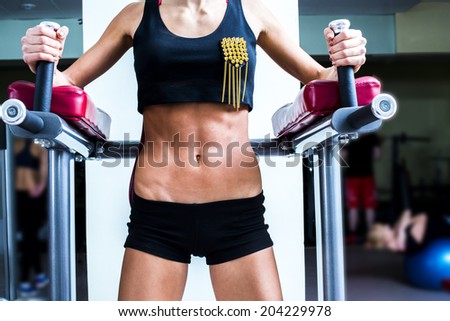 Fitness cut slim Woman in black short shorts No face. Close-up young adult blond girl  holding simulator for swing press and muscles sexy legs on dark green wall background Abdominal Exercises