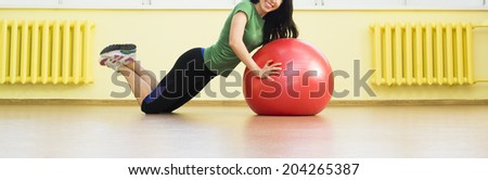 girl doing crunches in the gym.  cute sexy fitness girl in gym dress based on red rubber ball near yellow wall and window Beautiful latin hispanic woman laying on the splits Copy space for inscription