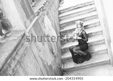 Full length Portrait of Beautiful caucasian blond woman sitting on concrete old retro vintage abandoned ladder or stairway along fence in perspective Empty Copy Space for inscription