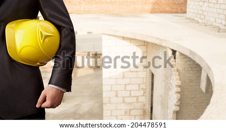 torso engineer or worker holding in hand yellow helmet for workers security over empty new building inside concrete and red brick wall inside house background Copy Space for inscription