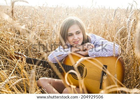 Portrait of Country latin hispanic girl sitting and dreaming with acoustic guitar at sunset golden wheat field Copy space for inscription Cute beautiful woman looking far away