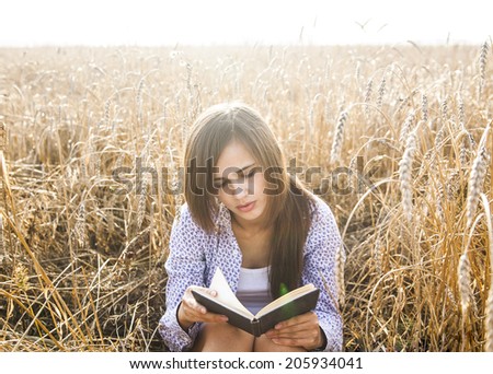 Portrait of young girl sitting on golden reap wheat in yellow sunset field Woman holding in hands black intresting book, reading text Empty Copy space for inscription Sun rays on brunette long hair
