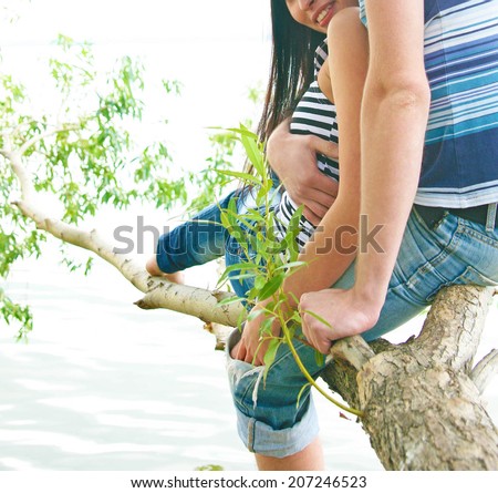 Image of Young adult couple in love sitting and embracing on a tree branch above the river water in nice sunny day. Empty copy space for inscription No face Unrecognizable person
