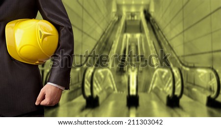 torso engineer or worker hand holding yellow helmet for workers security against the background of escalator  in shop perspective Empty copy space for inscription