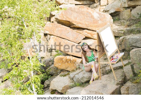 Young artist girl painting an summer landscape near clear water Woman sitting on stone mountain beach Empty copy space for inscription