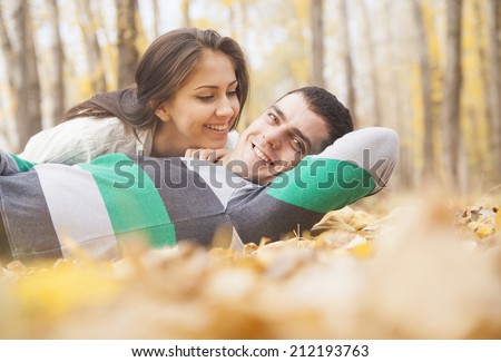 portrait of young adult Beautiful latin hispanic couple lying on fresh yellow autumn leaves kissing and hugging Cute pair people looking at each other on fall trees in city park background