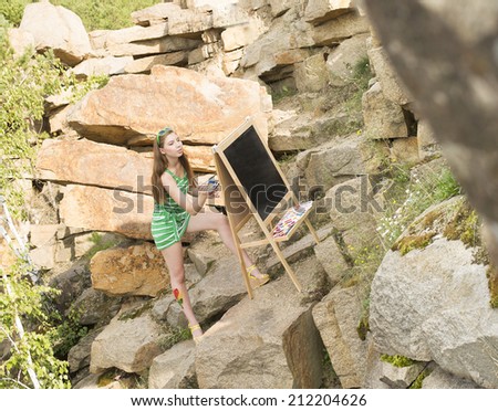 Portrait of Young adult artist girl painting an summer landscape near clear water Woman sitting on stone mountain beach Empty copy space for inscription