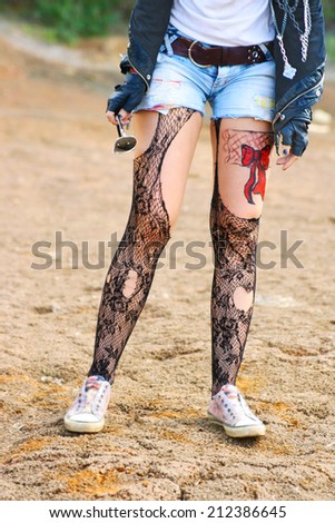 woman legs painted body art in the form of red bow in t-shirt and denim shorts and torn pantyhose on the background of desert No face Unrecognizable person