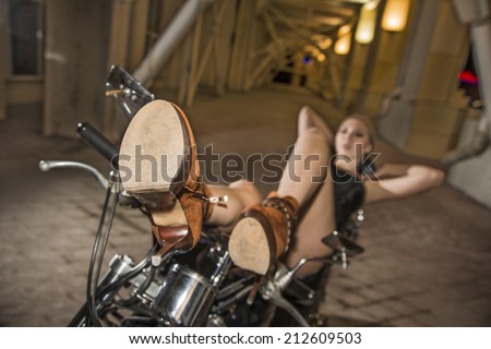 Focus on brown shoes Sexy girl lies on a motorcycle arch in dark room Dreaming fashion woman with long slim sexy legs wearing black leather jacket and short jeans shorts
