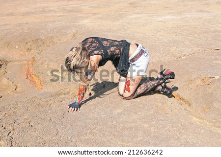 freak tattoo girl with bat and with body art on her hand on empty land desert background woman painted body art in form of fire in black transparent shirt and jeans shorts and torn pantyhose No face