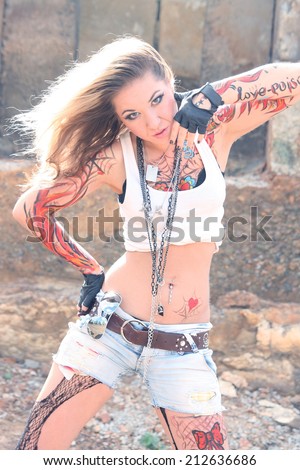 Portrait of freak woman painted body art in form of fire in white shirt jeans shorts torn black pantyhose on background of industrial abandoned vintage grunge buildings, old concrete wall Copy space