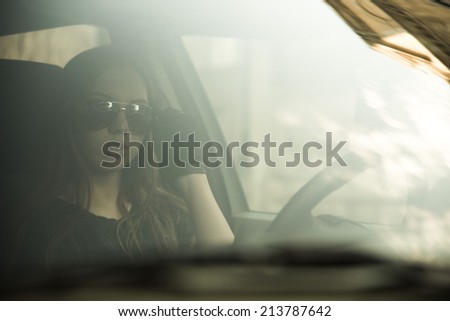 woman in car indoor keeps wheel turning around serious looking idea taxi driver holding stylish sunglasses in hands with leather black gloves against sun set sky background Copy space for inscription