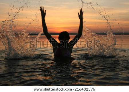 Silhouette of a girl spraying in lake at summer sunset cloudy sky background Face and hands of woman playing with splash of water Reflection on texture water
