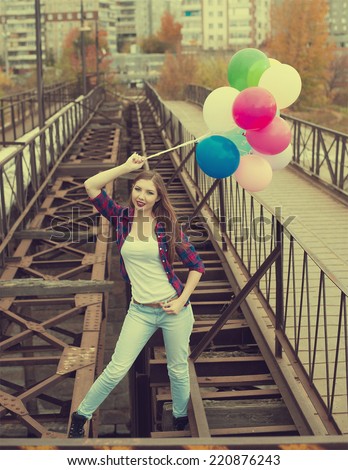 Full length Portrait of Happy woman with colorful balloons standing on old retro vintage metal bridge in perspective Young adult girl wearing casual dress Looking at camera against houses