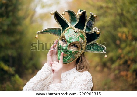 Portrait of Beautiful woman in green carnival mask with metal bells . Photo against autumn forest park  background.Fall trees blurred backdrop Idea and sign