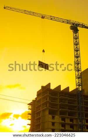 crane lifts the concrete plate load on a house under construction in the background of a sunset.vertical shot against sunset sky background with evening sun Empty copy space for inscription