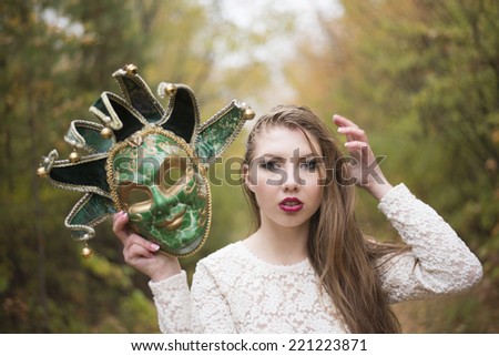 Beautiful woman in green carnival mask with metal bells .against autumn forest park background.Fall trees blurred backdrop Idea duplicity double game sham pretense hypocrisy postiche dissimulation
