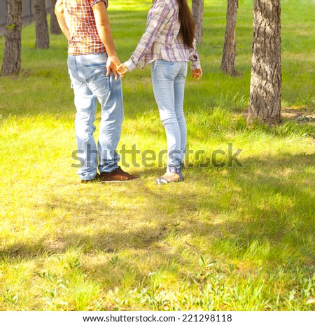 Unrecognizable person, no face, young couple holding hands wearing jeans Man and woman against fresh green grass and trees in perspective in sunny light bright park Empty copy space for inscription