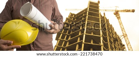 engineer yellow helmet for workers security on background of new high-rise apartment buildings and construction cranes and evening sunset sky Copy space for inscription No face Unrecognizable person