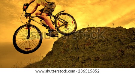 no face Unrecognizable person Silhouette of a man on mountain bike jumping in air on big stone  against sunset yellow sky with dramatic clouds background texture Empty copy space for inscription