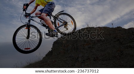 no face Unrecognizable person Silhouette of a man on mountain bike jumping in air on big stone  against sunset yellow sky with dramatic clouds background texture Empty copy space for inscription