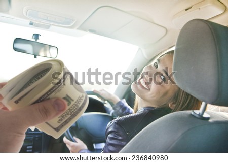 woman in car indoor keeps wheel turning around smiling looking at passengers in back seat idea taxi driver talking to hand hold money dollar who asks for directions right to drive Documents exam