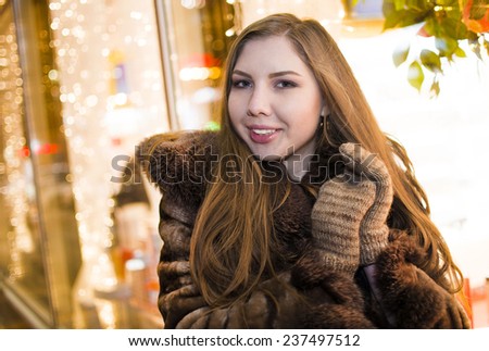 portrait of girl looking on camera shopwindow Lady woman wear wool gloves brown hair lie on fur collar coat Female wearing luxary winter dress Outdoor outside night city life style light background