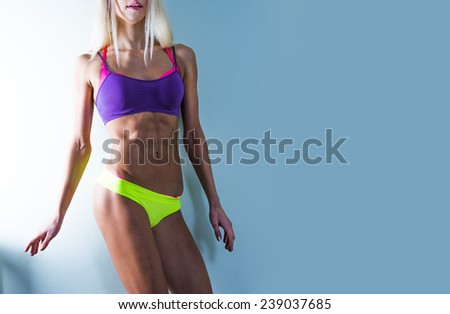Colorful of blonde bodybuilder young adult sexy girl with long hair Portrait of slim sporty cut VERY HOT woman standing against gray TEXTURED WALL Copy space for inscription flat stomach with press