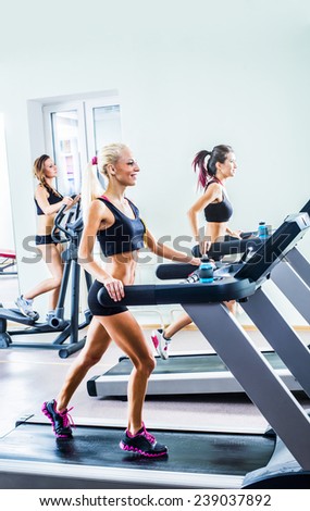 Three young adult sporty women run on machine in  gym centre sport slim sexy girl friends on Treadmill running inside in fitness gym Empty copy space for inscription