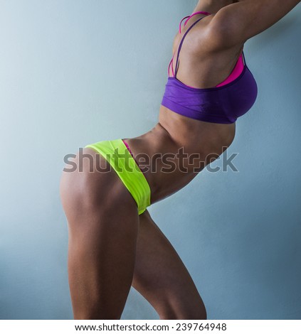 Colorful of bodybuilder young adult sexy girl with long hair Portrait of slim sporty cut VERY HOT woman standing against gray TEXTURED WALL Copy space for inscription flat stomach with press No face