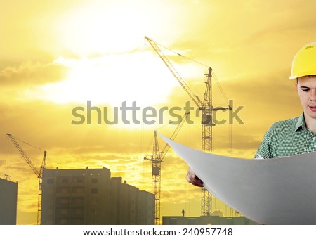 engineer hold blue print paper document wear helmet for workers security on background of new highrise buildings construction cranes on background evening sunset cloudy sky Silhouette Crane lifts load