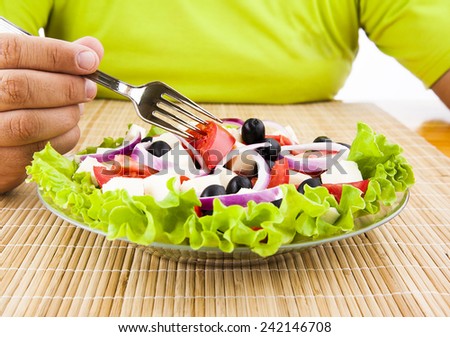 man hand hold fork with red fresh tomatoes under glass transparent plate with greek healthy salad with green leaf round onion black olive cheese Male no face unrecognizable person eating health food