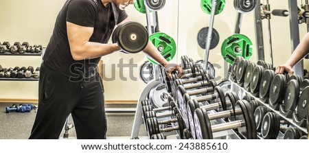 No face Unrecognizable person dumbbells in health club on metal shelf with young adult man lifting weights in mirror reflection on yellow wall texture background Empty space for inscription