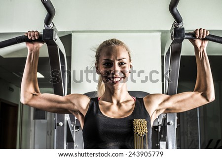 Portrait of Fitness Woman with smiling face looking at camera. Close-up young adult blond girl with long hair holding simulator for swing press expressed muscles in arms on dark green wall background