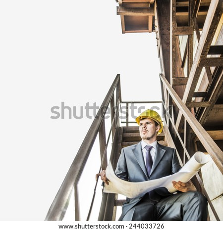 Portrait young adult caucasian male architect builder in yellow hardhat looking paper plan blueprint documents. Horizontal shape front view Serious Well dressed engineer sitting on metal rusty ladder