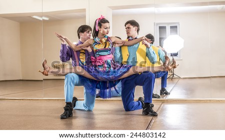 Funny dancer three people Two man one woman dressed in boogie-woogie rock\'n\'roll pin up style posing together in studio against mirror reflection Girl sit on splits on gays  knees Colorful costumes