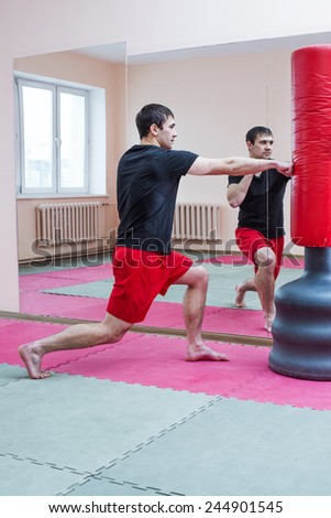 Portrait of young adult latin hispanic man boxer training in gym boxing red standing punching bag with reflection in mirror Aggressive male inside wall room against window background
