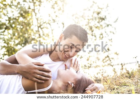 Portrait of Young adult beautiful couple lying on green yellow dry grass and look each other. Sunset rays light sky against summer trees background Empty space for inscription  or object