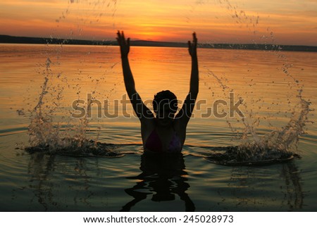 Silhouette of a girl spraying in lake at summer sunset cloudy sky background Face and hands of woman playing with splash of water Reflection on texture water