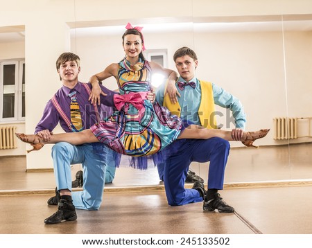 Funny dancer three people Two man one woman dressed in boogie-woogie rock\'n\'roll pin up style posing together in studio against mirror reflection Girl sit on splits on gays knees Colorful costumes