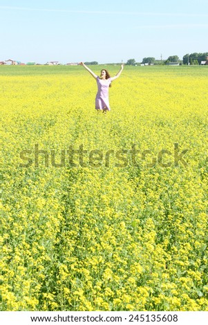 redhead curly young adult woman in yellow raps spring summer flower field and blue  sky with clouds background Copy space for inscription Girl wearing violet sexy dress Hands up