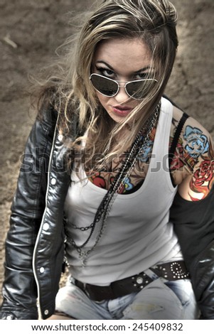 Portrait of stylish tattoo woman painted body art in form of blue flower in shirt, ta too Girl wearing black leather jacket holding sunglasses on texture background Empty copy space for inscription