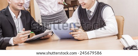 No face Unrecognizable person Three business people sitting at table with paper plan document near landline phone and planning hard work against wooden door in wall background Woman stand between mens