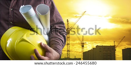 engineer hold yellow helmet for worker security blue print paper document on background of highrise apartment buildings and construction cranes on background of sunset sky Silhouette Crane lifts load