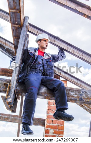Full length body portrait of worker on a steel beam raises his hands sitting on rusty structure metal beam - roof frame, Under construction on blue summer sky background with clouds